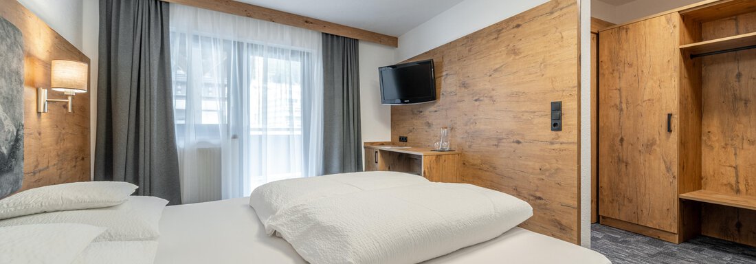 A modern hotel room with a box spring bed. The room is bright and inviting, with a television, an open wardrobe, and a balcony. - Apart Hotel Garni Alt Kaisers - Sölden