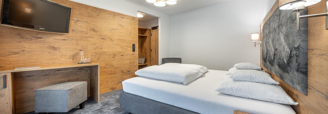 A modern bedroom with a comfortable box spring bed and wooden decor. The room is well-lit and cozily furnished. - Apart Hotel Garni Alt Kaisers - Sölden