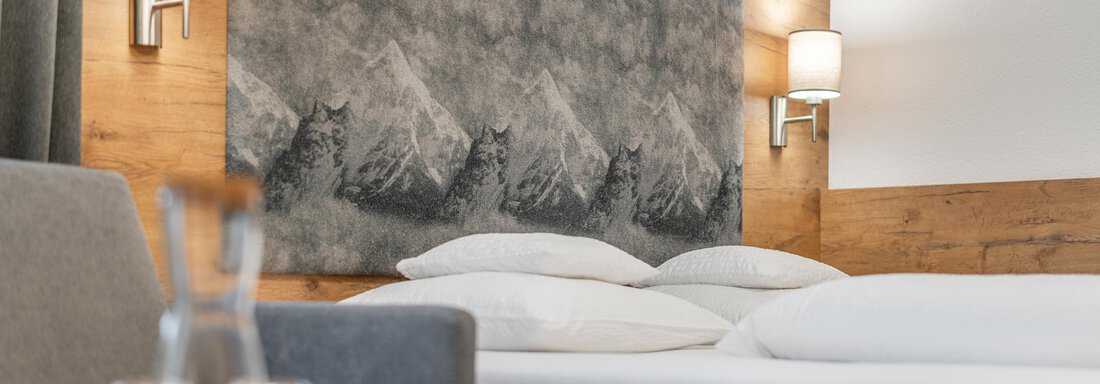 A modern bedroom with a large box spring bed and artistic wall design. Warm wood and soft lighting create an inviting atmosphere. - Apart Hotel Garni Alt Kaisers - Sölden