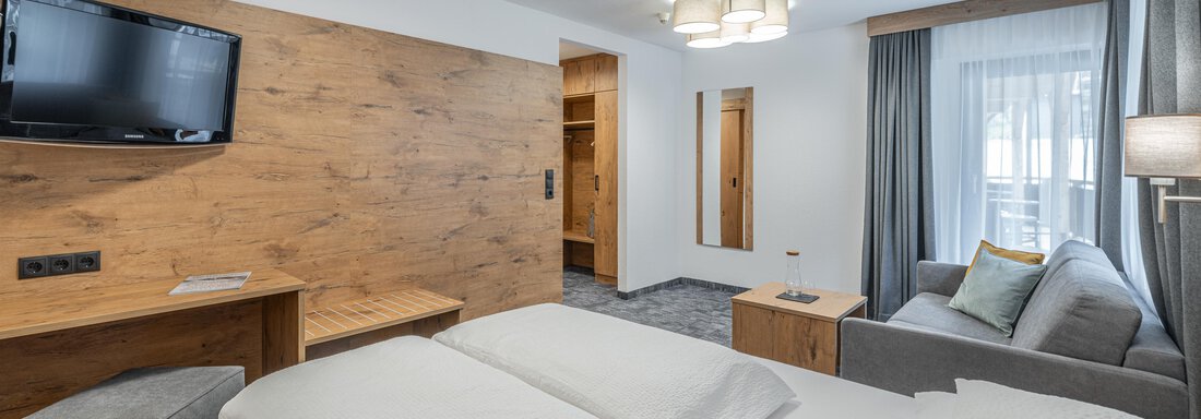A modern hotel room with a box spring bed, a television, and a cozy seating area. The room has large windows that let in plenty of light. - Apart Hotel Garni Alt Kaisers - Sölden