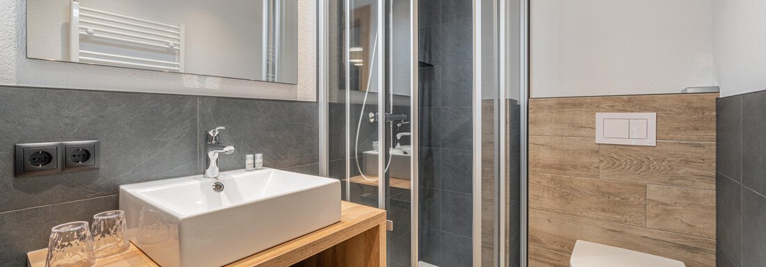 A modern bathroom with a walk-in shower and an elegant sink. The floor is elegantly tiled and provides a pleasant contrast to the wooden shelves. - Apart Hotel Garni Alt Kaisers - Sölden
