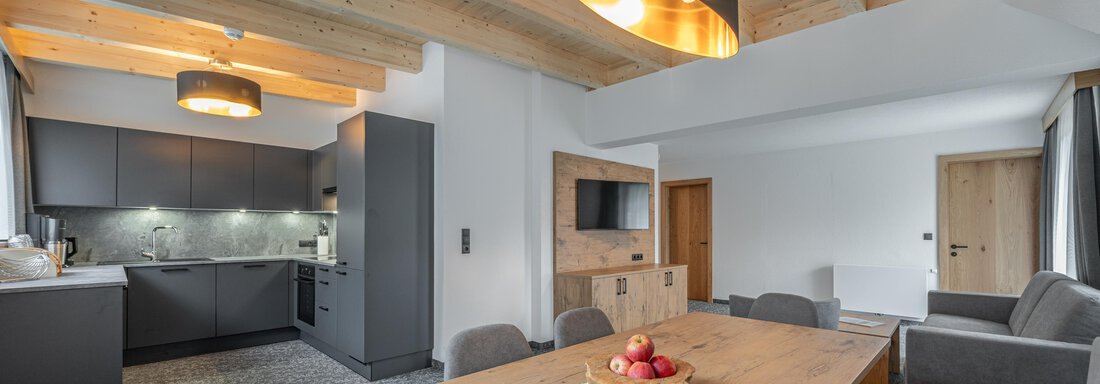 web-alt-kaisers-app-21-6999 A modern living room with an open kitchen area and a large wooden dining table. The stylish decor includes bright wooden ceilings and cozy furniture. - Apart Hotel Garni Alt Kaisers - Sölden