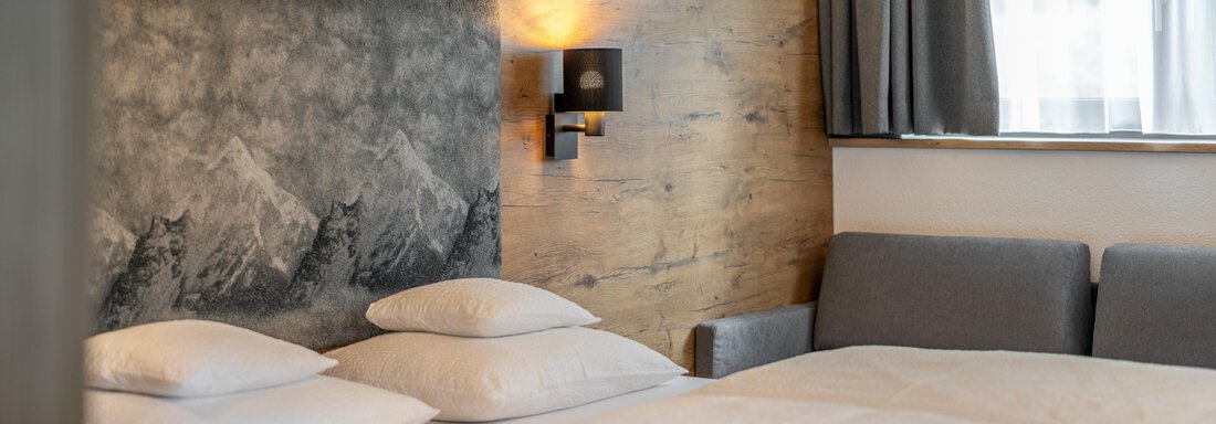 A modern bedroom with two beds, white bedding, and a cozy atmosphere. The walls are partially made of wood, and there is stylish lighting and windows with curtains. - Apart Hotel Garni Alt Kaisers - Sölden