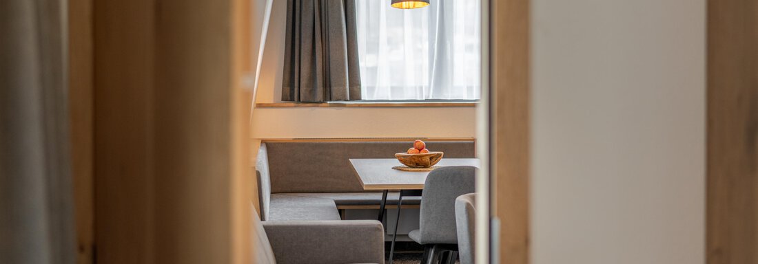 An inviting living space with comfortable furniture and a large window. A table with fresh fruit is at the center of the room. - Apart Hotel Garni Alt Kaisers - Sölden