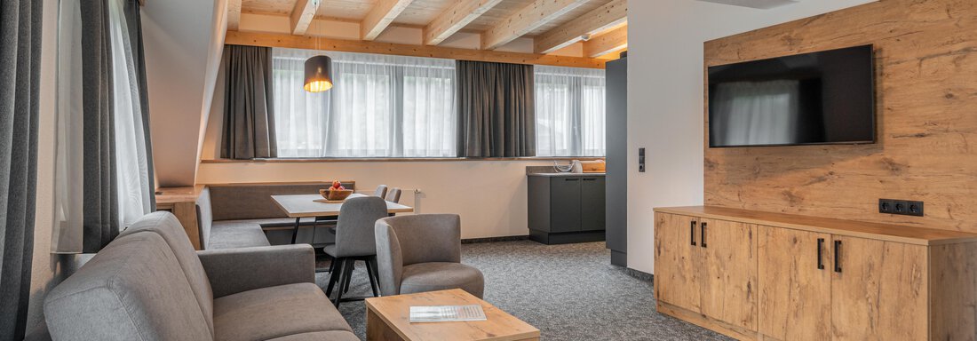 A modern living and dining room with a cozy seating area and a wooden table. Large windows provide plenty of daylight and a pleasant atmosphere. - Apart Hotel Garni Alt Kaisers - Sölden