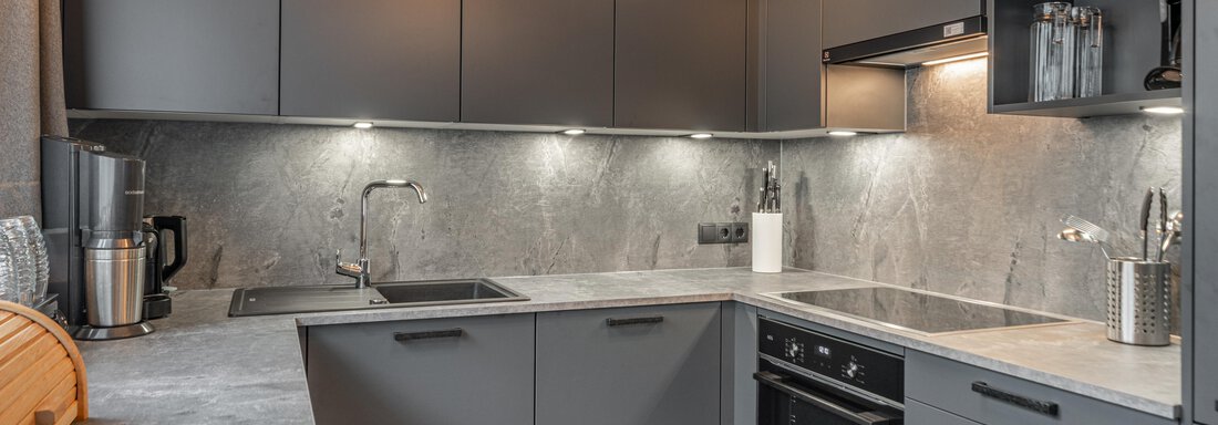 A modern kitchen with gray cabinets and an elegant countertop. The lighting creates a bright and inviting atmosphere. - Apart Hotel Garni Alt Kaisers - Sölden