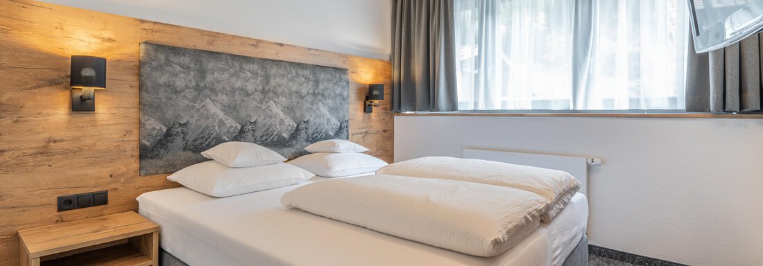 A modern bedroom with a double bed and wooden paneling. Large windows let in plenty of light and create a bright atmosphere. - Apart Hotel Garni Alt Kaisers - Sölden