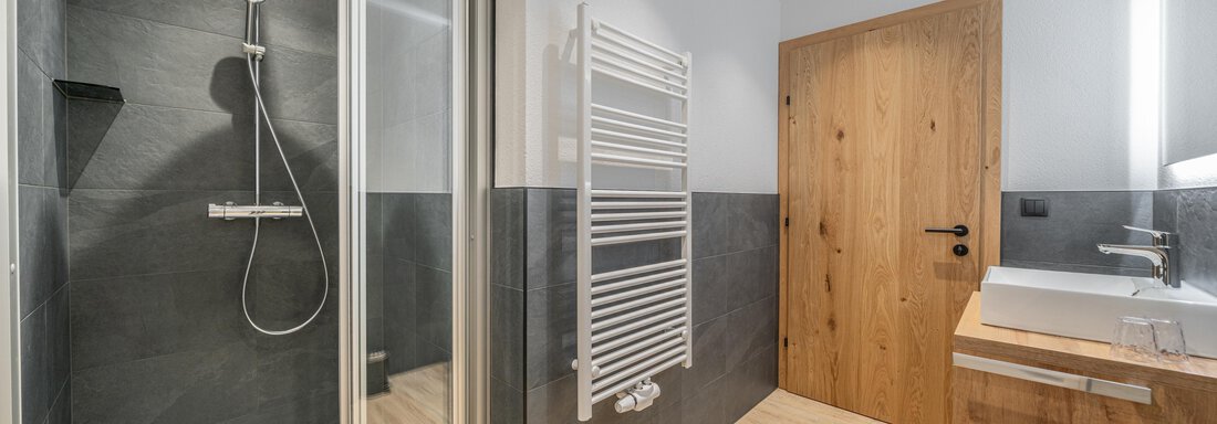 A modern bathroom with a shower and a wooden washbasin. The walls are in neutral tones, and the floor is made of wood. - Apart Hotel Garni Alt Kaisers - Sölden