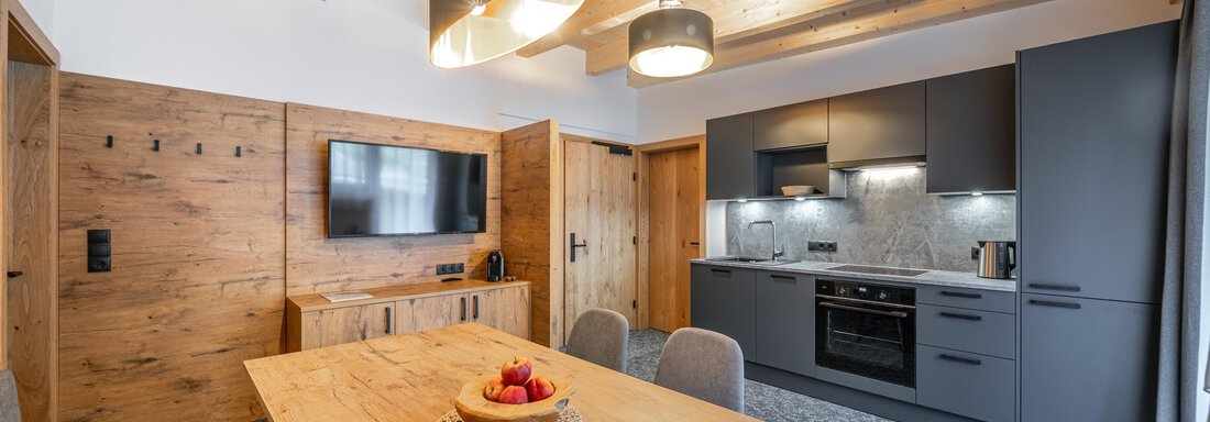 web-alt-kaisers-app-22-7015 A modern kitchen with wooden ceilings and a dining table. The space is bright and friendly, with elegant furniture and a television on the wall. - Apart Hotel Garni Alt Kaisers - Sölden