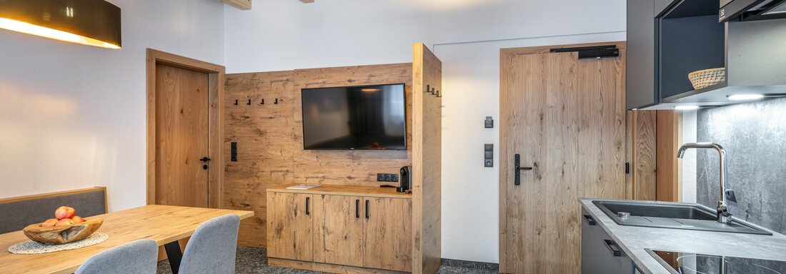 A modern apartment with wooden ceilings and stylish design. The living area includes a television, a dining table, and a well-equipped kitchen. - Apart Hotel Garni Alt Kaisers - Sölden