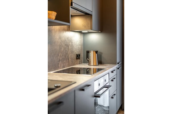 A modern kitchen with an elegant countertop and a stainless steel kettle. The walls are in dark tones, and the lighting creates a cozy atmosphere. - Apart Hotel Garni Alt Kaisers - Sölden