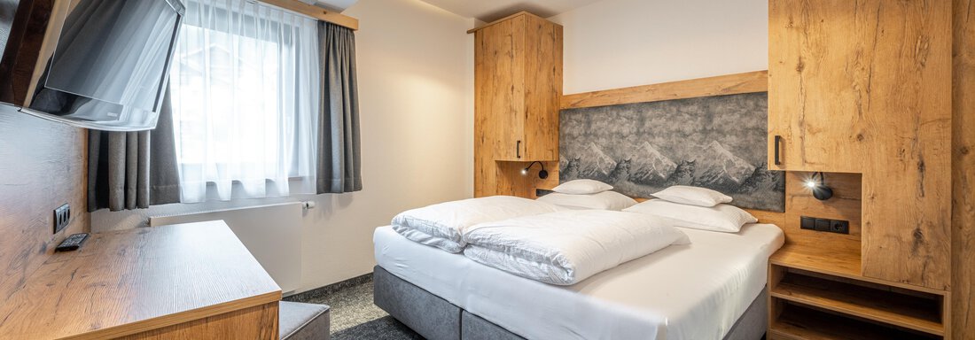 A modern room with a double bed and wooden furniture. A television and a large window create a bright and inviting atmosphere. - Apart Hotel Garni Alt Kaisers - Sölden