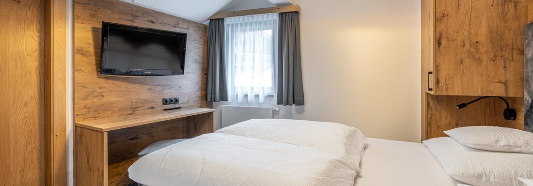 A modern bedroom with a double bed and wooden decor. There is a television and large windows that let in plenty of light. - Apart Hotel Garni Alt Kaisers - Sölden