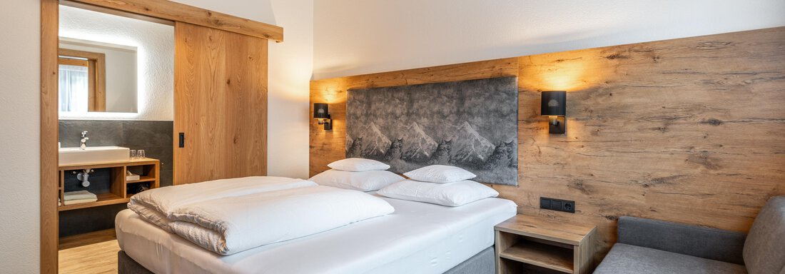 A modern bedroom with a double bed and wooden details. The room is bright and cozy, with a small sofa and an adjacent bathroom. - Apart Hotel Garni Alt Kaisers - Sölden