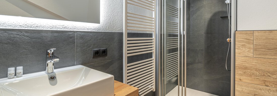 A modern bathroom with a shower and an elegant sink. The walls are done in neutral tones, and there are wooden details. - Apart Hotel Garni Alt Kaisers - Sölden
