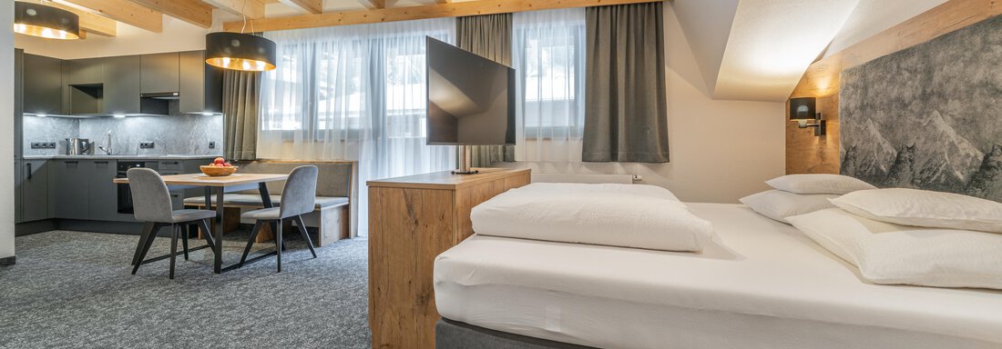 Appartement 23 | © Johannes Brunner (CC C) A modern studio with a box spring bed and a cozy seating area. The wooden ceiling and windows create a bright, inviting, and cozy atmosphere. - Apart Hotel Garni Alt Kaisers - Sölden