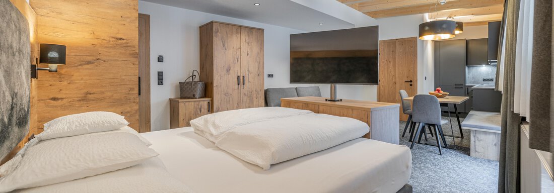 A modern and stylish room with a large box spring bed and wooden decor. The room features a seating area and a cozy atmosphere. - Apart Hotel Garni Alt Kaisers - Sölden