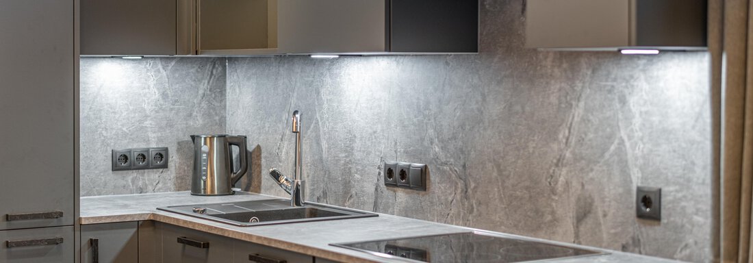 A modern kitchen with gray cabinets and a sleek countertop. The lighting creates a cozy atmosphere. - Apart Hotel Garni Alt Kaisers - Sölden