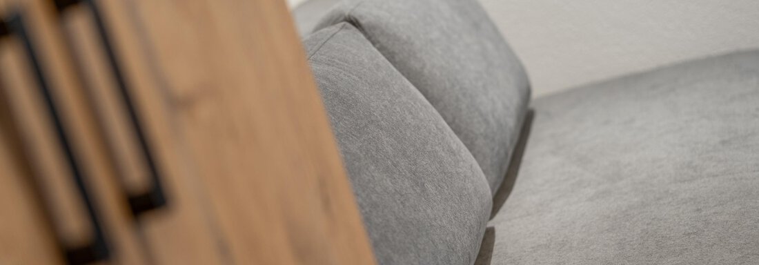 A gray sofa with soft cushions is visible in the picture. In the background, a wooden cabinet is suggested. - Apart Hotel Garni Alt Kaisers - Sölden
