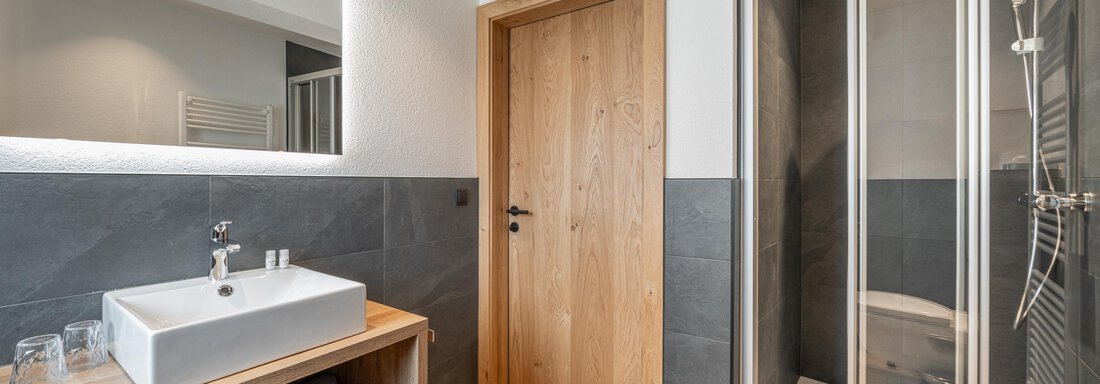 A modern bathroom with a shower and wooden details. The sink is mounted on an elegant wooden cabinet. - Apart Hotel Garni Alt Kaisers - Sölden