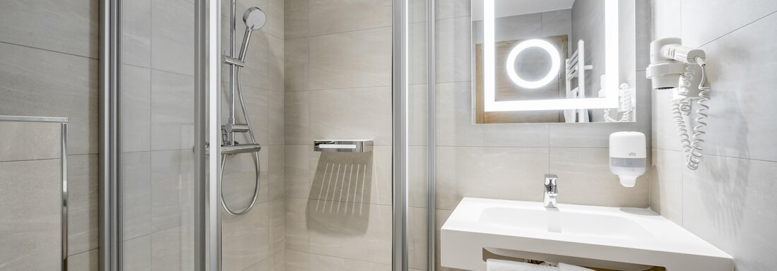 A modern bathroom with a shower and a sink. The walls are brightly tiled, and a backlit mirror provides additional light. - Apart Hotel Garni Wieser - Sölden