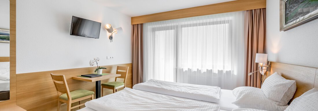 A bright, modern room with two single beds. There is a table with chairs and a TV set on the wall. - Apart Hotel Garni Wieser - Sölden