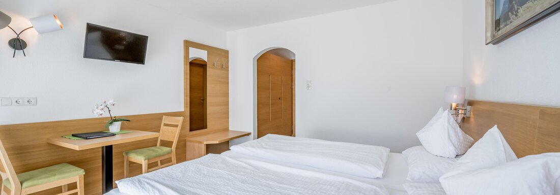 A modern hotel room with a double bed, a table, and chairs. It features a television and soft lighting. - Apart Hotel Garni Wieser - Sölden