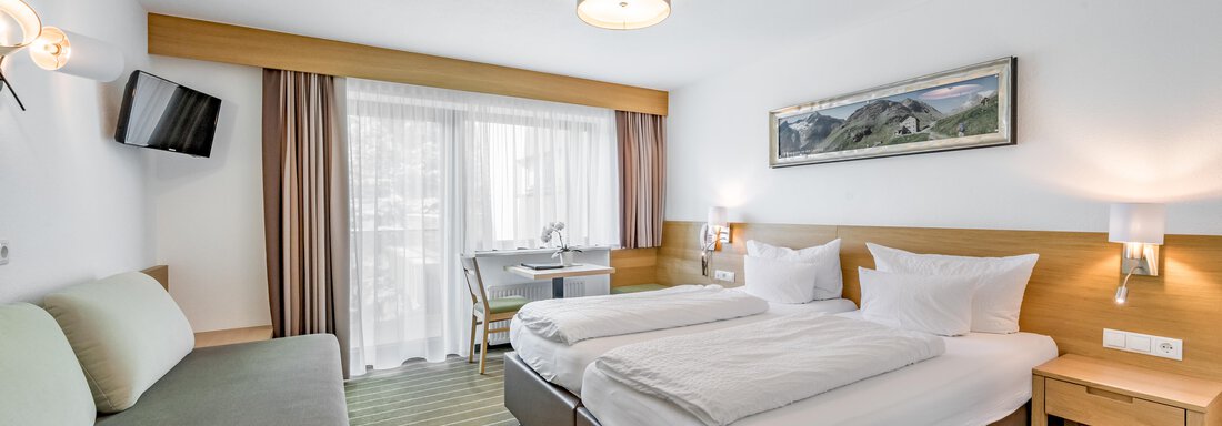 A modern hotel room with two single beds and a cozy sofa. Large windows provide plenty of daylight and a pleasant atmosphere. - Apart Hotel Garni Wieser - Sölden