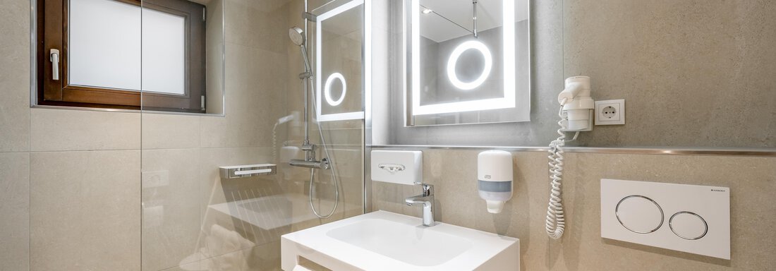 A modern bathroom with a glass shower cabin and an elegant sink. The mirrors are equipped with LED lights and the walls are in neutral colors. - Apart Hotel Garni Wieser - Sölden