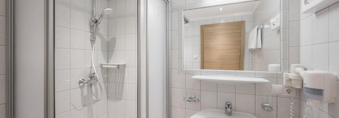 A modern bathroom with a shower and a sink. The walls are tiled with bright tiles, and a mirror reflects the space. - Apart Hotel Garni Wieser - Sölden
