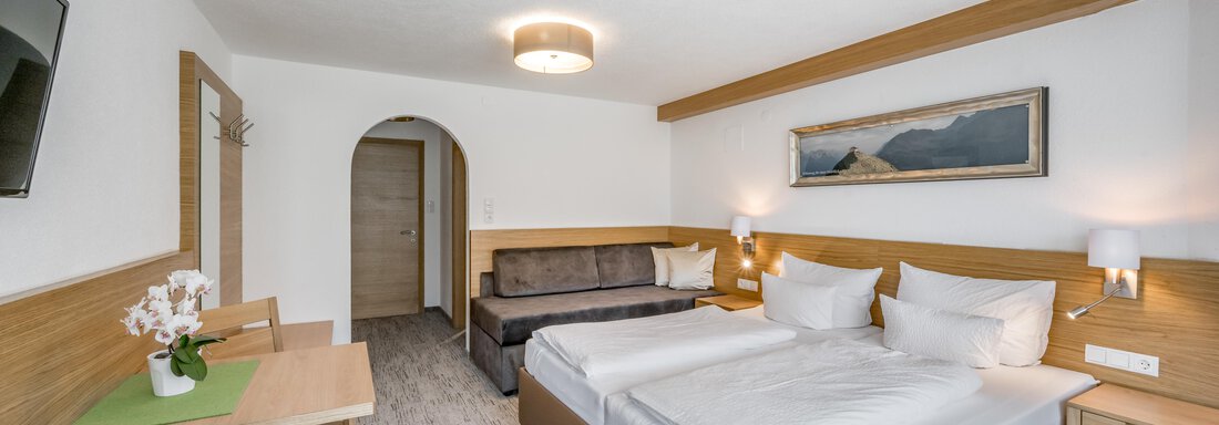 A modern hotel room with two single beds and a cozy sofa. There is a table, a television, and subtle decoration. - Apart Hotel Garni Wieser - Sölden