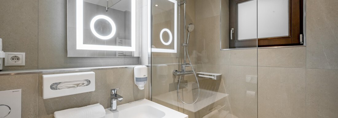 A modern bathroom with a sink, a large mirror, and a shower. Natural light streams in through a window and the walls are painted in neutral tones. - Apart Hotel Garni Wieser - Sölden
