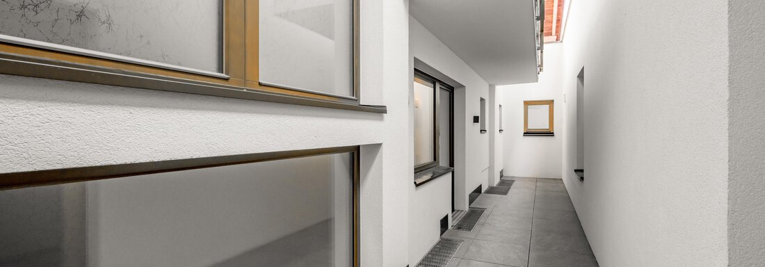A narrow, modern corridor with bright walls and large windows. The floor is covered with gray tiles, and the atmosphere is calm and minimalist. - Apart Hotel Garni Wieser - Sölden