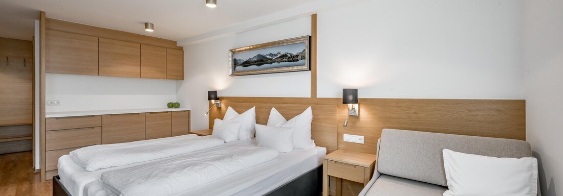 A modern bedroom with a double bed and a cozy sofa. The walls are light and the furniture is made of wood, creating a warm atmosphere. - Apart Hotel Garni Wieser - Sölden