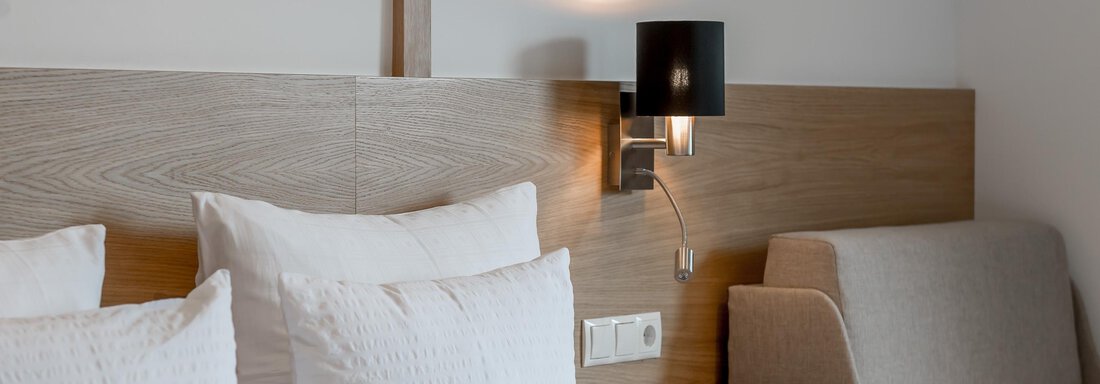 A modern bedroom with two bed cushions and a cozy seating area. The walls are in warm, light tones, and a wall lamp provides pleasant lighting. - Apart Hotel Garni Wieser - Sölden