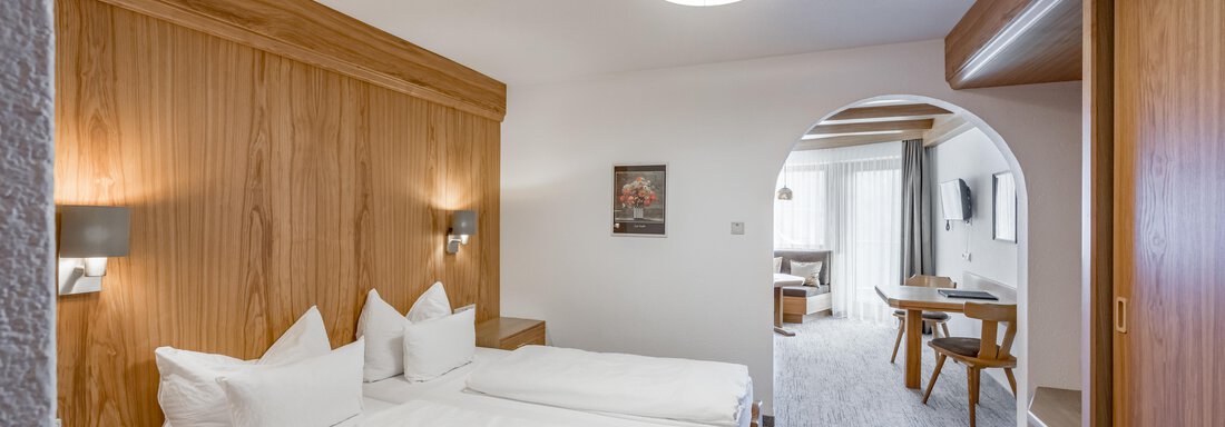 A modern hotel room with two single beds and warm wood decor. In the background, there is a cozy seating area and a window with curtains. - Apart Hotel Garni Wieser - Sölden