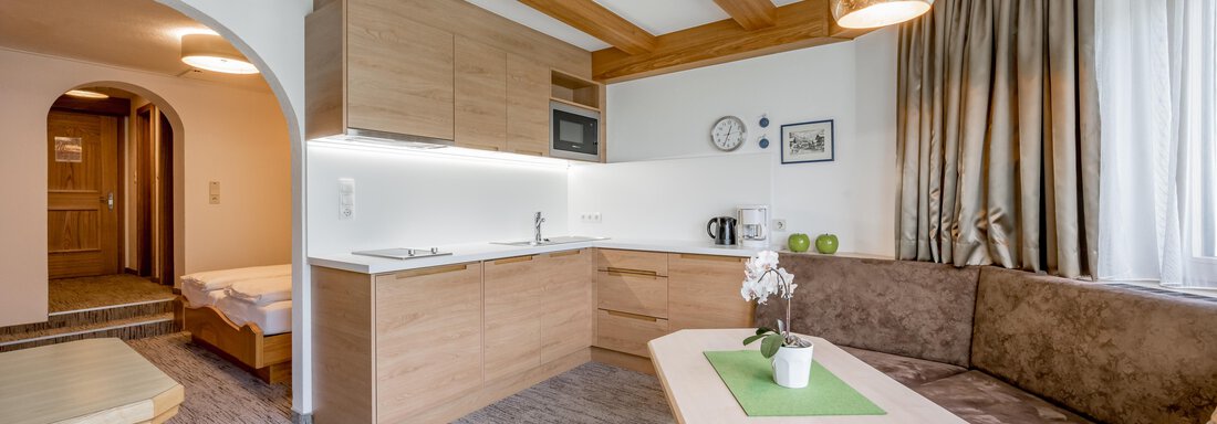 A modern kitchen with wooden shelves and a cozy seating area. The room design is bright and welcoming, perfect for social gatherings. - Apart Hotel Garni Wieser - Sölden