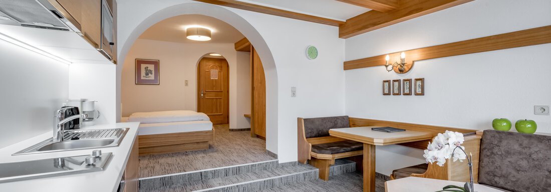 A modern vacation apartment with a fully equipped kitchen and a cozy dining area. The wooden ceiling and appropriate lighting create an inviting atmosphere. - Apart Hotel Garni Wieser - Sölden