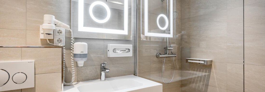 A modern bathroom with an elegant vanity and illuminated mirrors. The walls are in a neutral beige, and there is a glass shower. - Apart Hotel Garni Wieser - Sölden