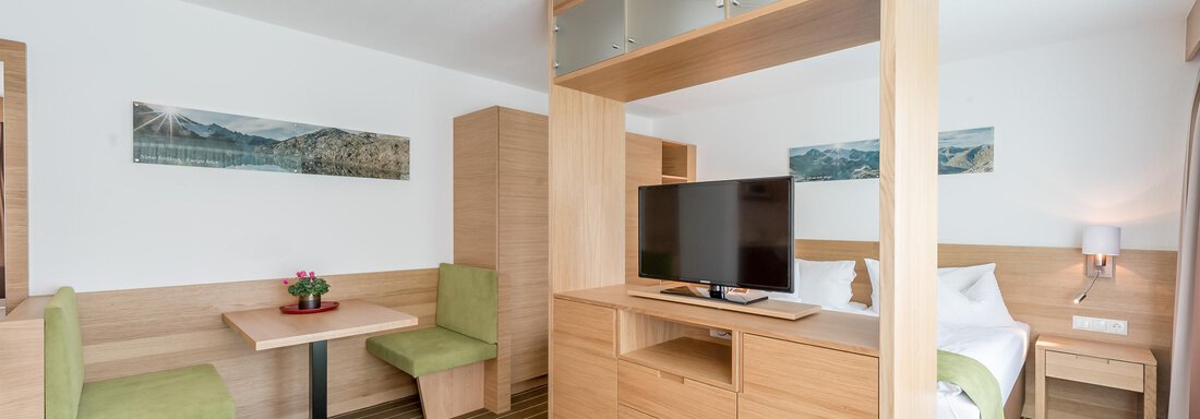 A modern hotel room with wooden interior. There is a table with chairs, a television, and a comfortable bed. - Apart Hotel Garni Wieser - Sölden