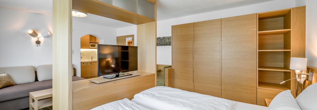 A modern hotel room with a double bed and a cozy seating area. The room is decorated in bright colors and features furniture made of light wood. - Apart Hotel Garni Wieser - Sölden