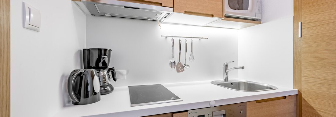 A modern kitchen with wooden cabinets and a white countertop. The amenities include a kettle, a microwave, and cooking utensils. - Apart Hotel Garni Wieser - Sölden
