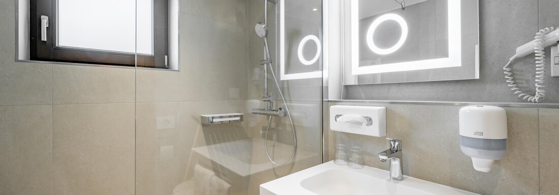 A modern bathroom with a shower and an elegant sink. The light is complemented by striking mirrors with lighting. - Apart Hotel Garni Wieser - Sölden