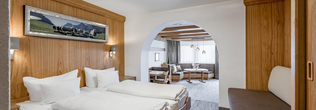 A modern hotel room with two beds and bright wood interior. A cozy living area is visible through an archway. - Apart Hotel Garni Wieser - Sölden