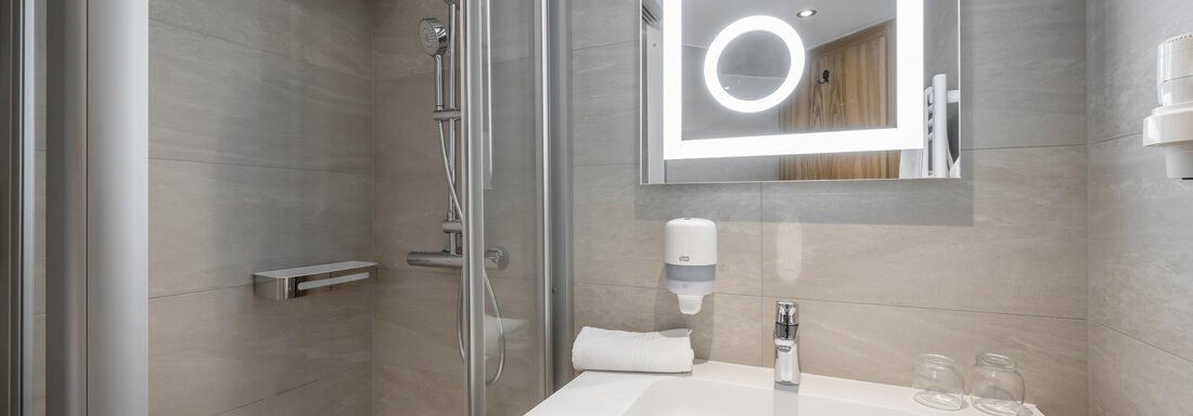 A modern bathroom with a shower and an elegant sink. The space is bright and clean, with a large mirror and hygienic amenities. - Apart Hotel Garni Wieser - Sölden