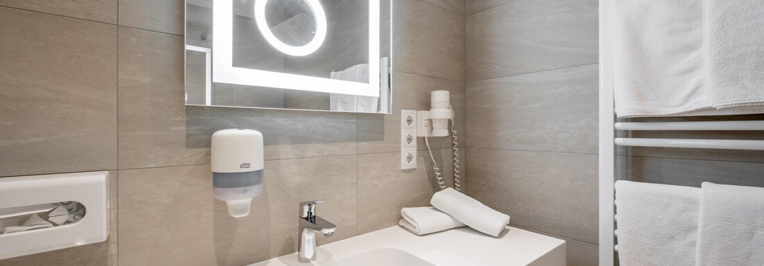 A modern bathroom with a sink and a illuminated mirror. Towels are neatly placed on a towel rack. - Apart Hotel Garni Wieser - Sölden