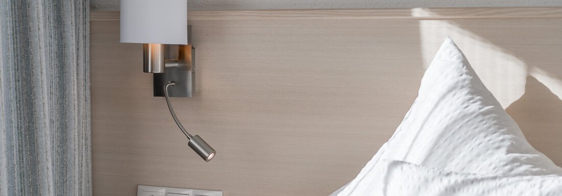 A cozy bedroom with a modern nightstand and a wall light. Pillows are neatly placed on the bed. - Apart Hotel Garni Wieser - Sölden