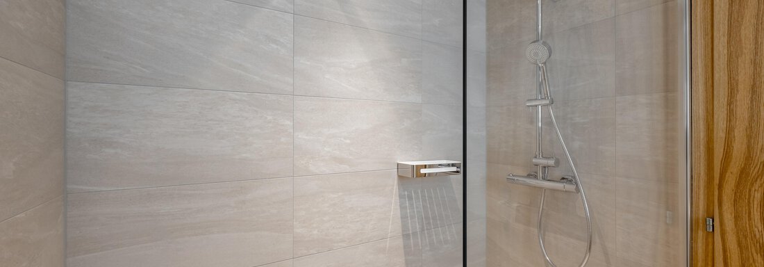 A modern shower with a glass partition. The walls are tiled in light gray tiles. - Apart Hotel Garni Wieser - Sölden