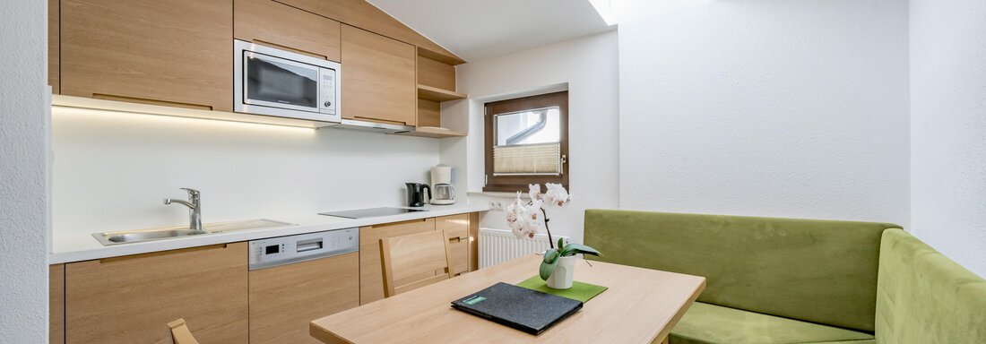 A modern kitchen with wooden cabinets and a cozy dining area. Light streams in through a skylight, creating an inviting atmosphere. - Apart Hotel Garni Wieser - Sölden