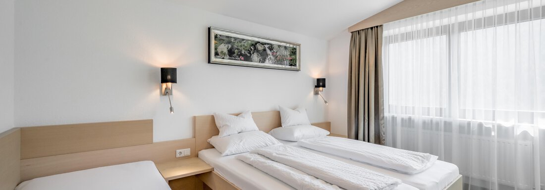 A modern bedroom with two single beds and an additional bed. Large windows ensure plenty of daylight and a bright atmosphere. - Apart Hotel Garni Wieser - Sölden